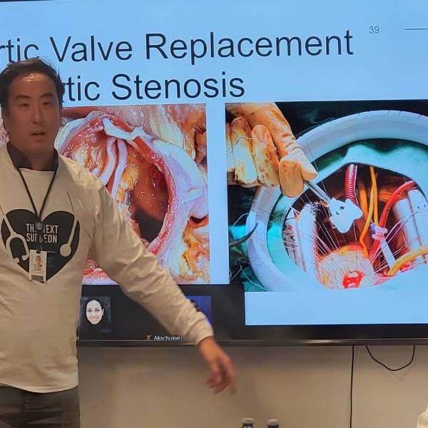 Dr. Robert Yanagawa standing in front of a PowerPoint presentation showing an aortic valve replacement operation.