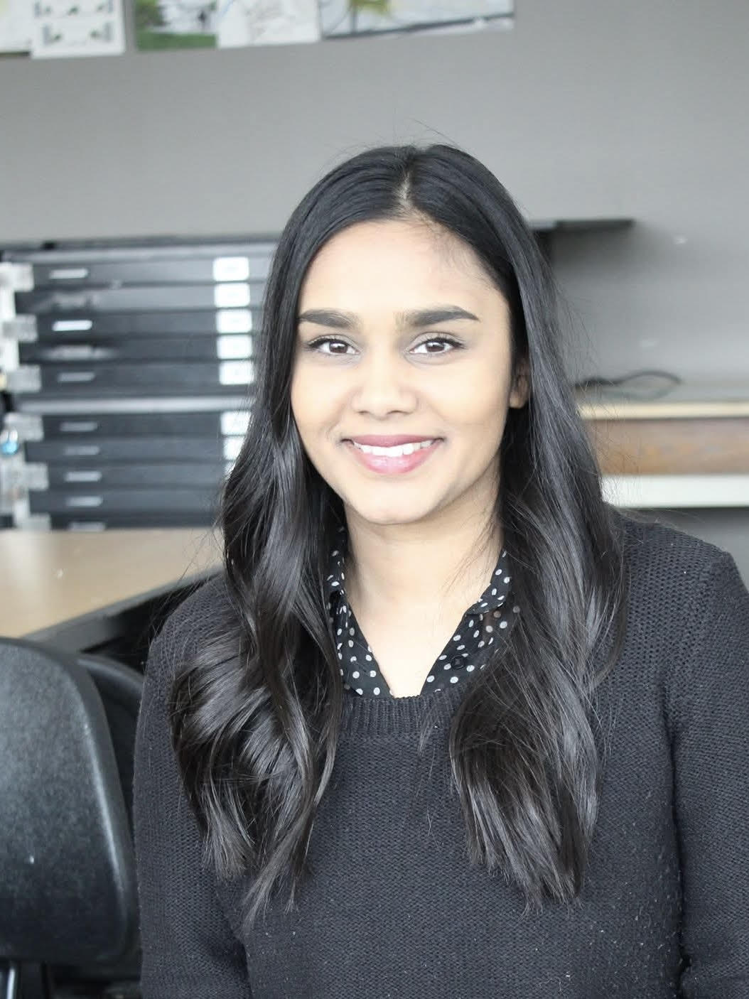 Woman dressed in a black sweater with a white polka dot collar standing in an office 