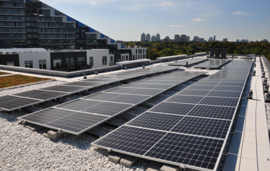 Photo of a building roof with three long black solar panels. Blue sky and a city skyline in the background