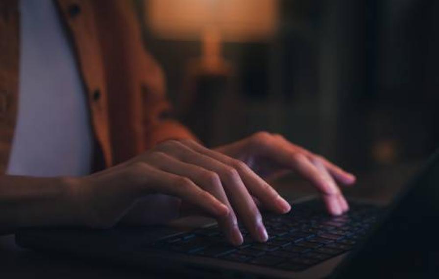 Hands typing on a computer. Lighting is dark. 
