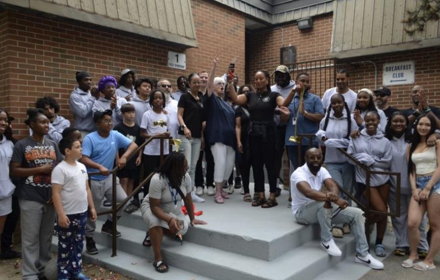 A group of people posing in front of a building while cutting a ribbon. 