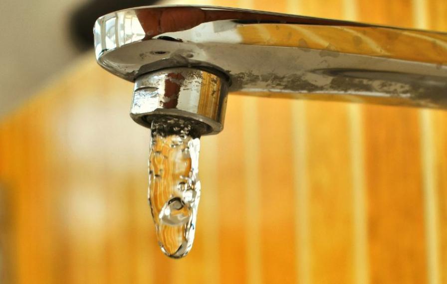 A close-up of a chrome faucet with water dripping from the spout against a blurred background of wooden paneling.