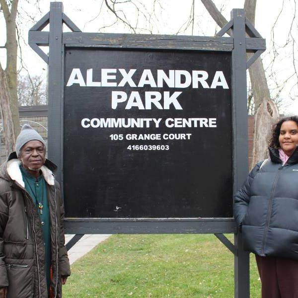 Two tenants in Alexandra Park, an artist and a poet, stand beside the Alexandra Park community centre sign.