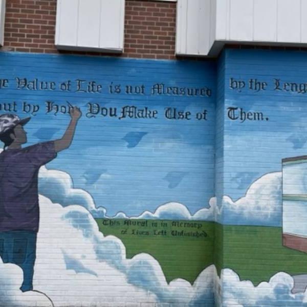 Mural on a brick wall in Alexandra Park community of a boy in clouds with the words 'The value of life is not measured by the length of days, but by how you make use of them'.