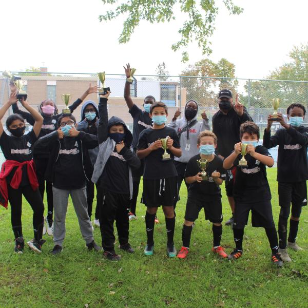 Group photo of TCHC staff and tenant youth wearing soccer outfits, cheering and holding up trophies