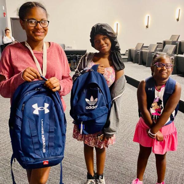 Three youth tenants show off their new backpacks. 