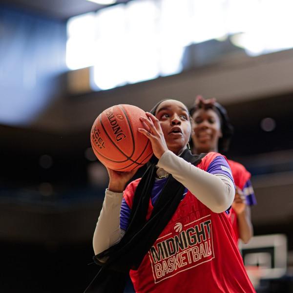 A girl wearing a red Midnight Basketball shirt prepares to throw the basketball at the net.