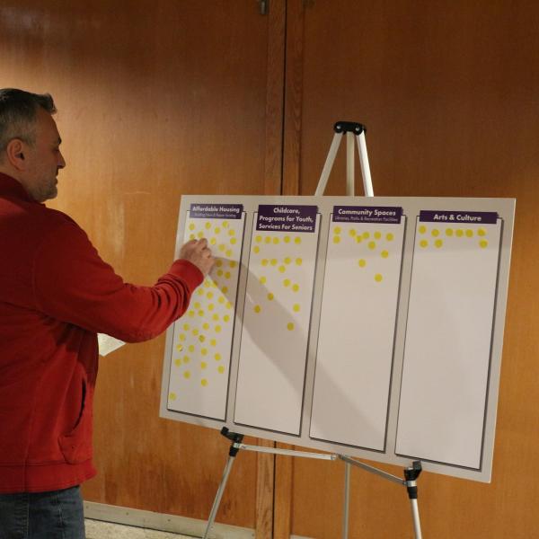 A male who is wearing a red sweater putting yellow dots on a board.