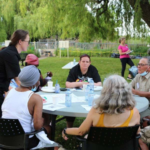 A group of people having a discussion around a table outdoors.
