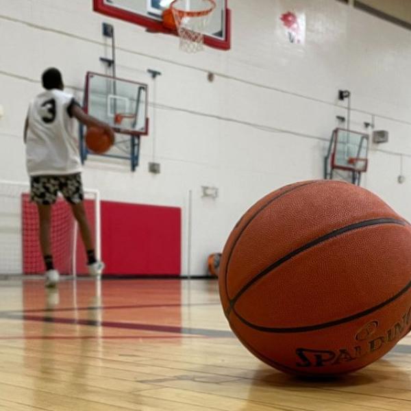 A basketball on a court with a young man practicing in the background. 