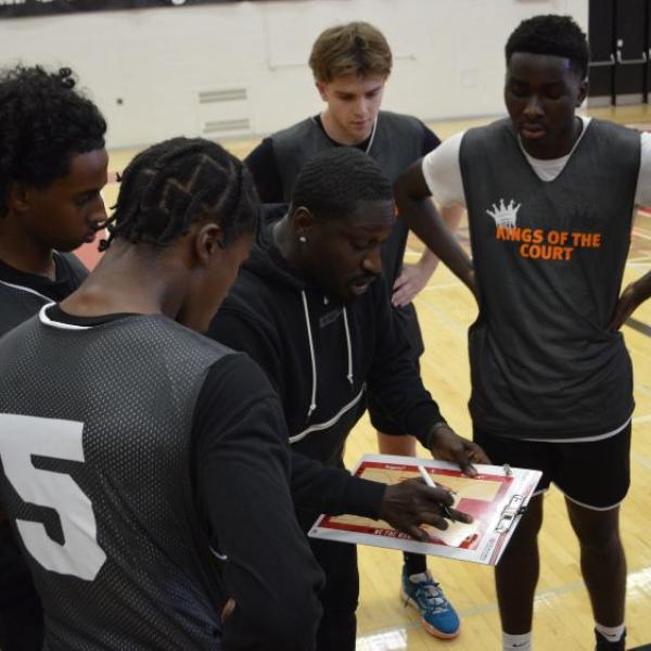 A person holding a clipboard reviewing the information while having players surround him. 