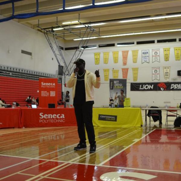 A man standing in a gym speaking to an audience.