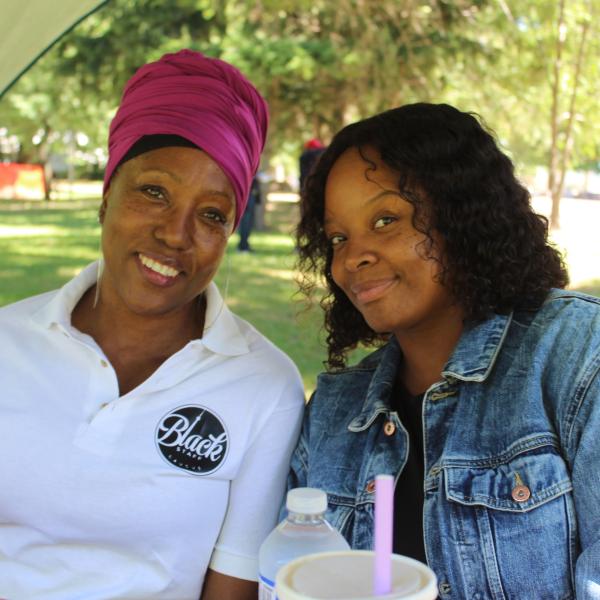 Two women sitting in shade during Black Staff Caucus barbeque.