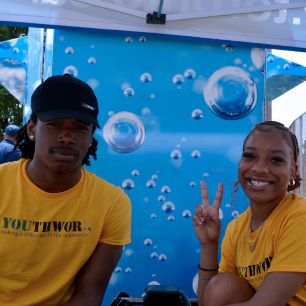 Two youth who are wearing yellow shirts sitting in front of the water cooling station.