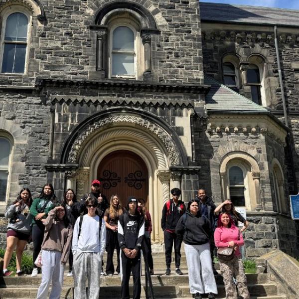 A group of people standing for a photo in front of a old building on an university campus