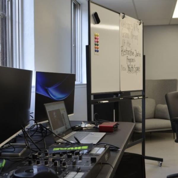 A photo of a room with a whiteboard, a laptop, monitors and studio equipment.