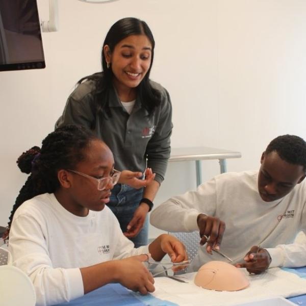 An instructor who is wearing a grey shirt is helping two youth work on a project in the lab.