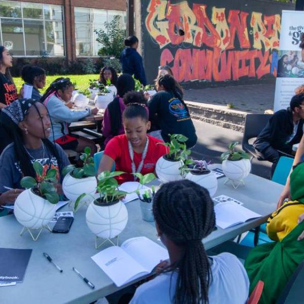 Girls sitting at a table on an outdoor court, painting basketball planters.