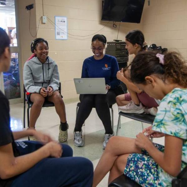 A group of girls sitting in a circle of chairs smiling and having a discussion.