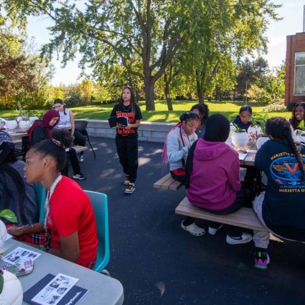 Girls sitting at various tables are set up on an outdoor court working on a painting craft.