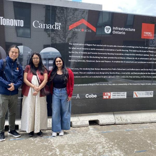A man, a woman and a woman standing in front of the Regent Park construction hoarding.