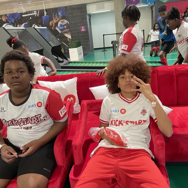 Two children in athletic wear posing on a red couch.