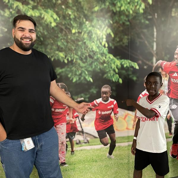 A child in athletic wear and a TCHC staff member posing in front of a mural depicting children playing soccer.