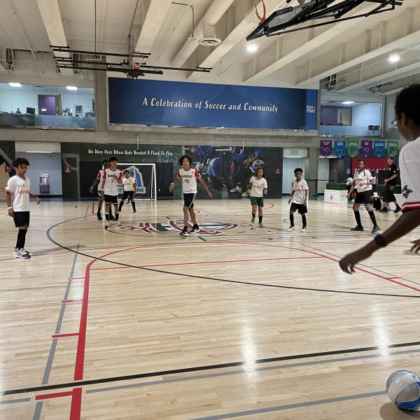A group of children playing soccer in a gymnasium.