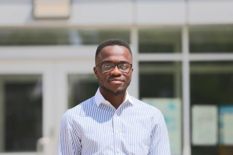 A photo of Stephen Mensah - a man wearing a collared shirt standing in front of a building.