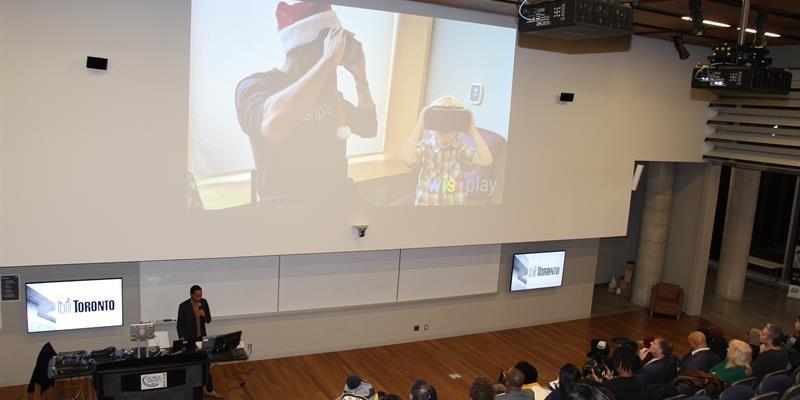 Man presenting in front of a crowd with a giant screen behind him