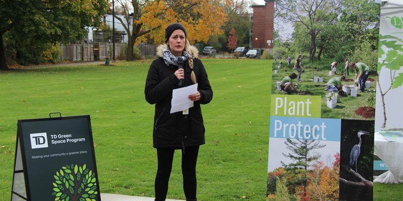 Woman holding a microphone standing in the park next to a banner