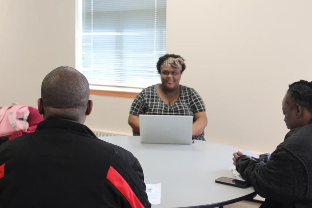 Alisha Griffith sitting at a table with a laptop, consulting with two other people who sit at the table with their backs to the camera.