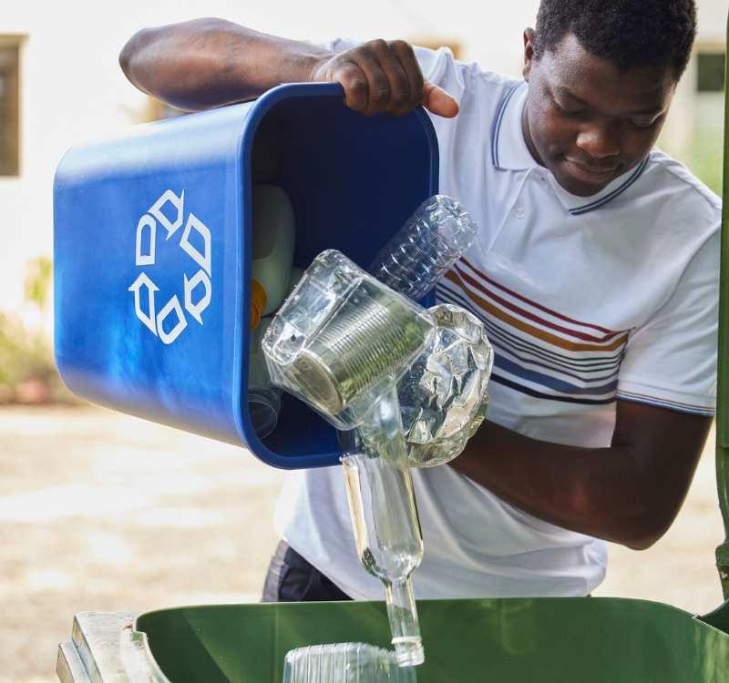 A young man recycling showing ways on how individuals can protect the globe. A young man recycling plastic into a green bin.
