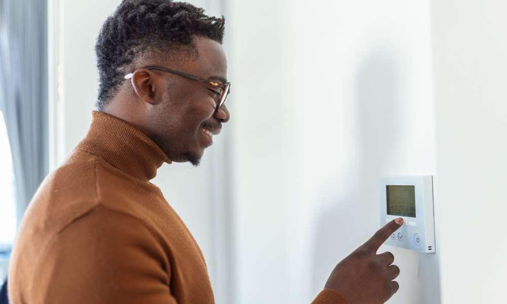 A man switching temperature by using the thermostat on the wall.