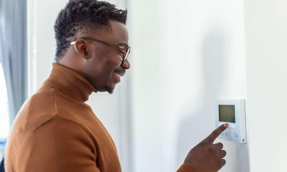 A man switching temperature by using the thermostat on the wall. 