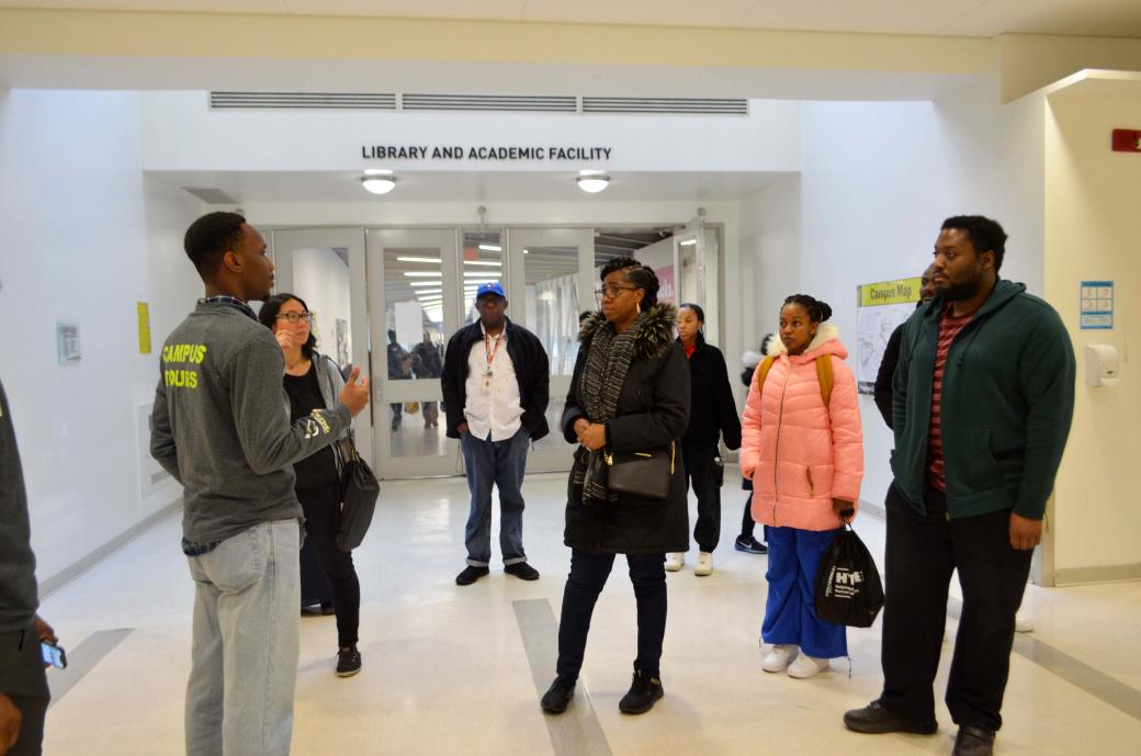 A group of people listening to tour guide speak in the hallways of a college campus.