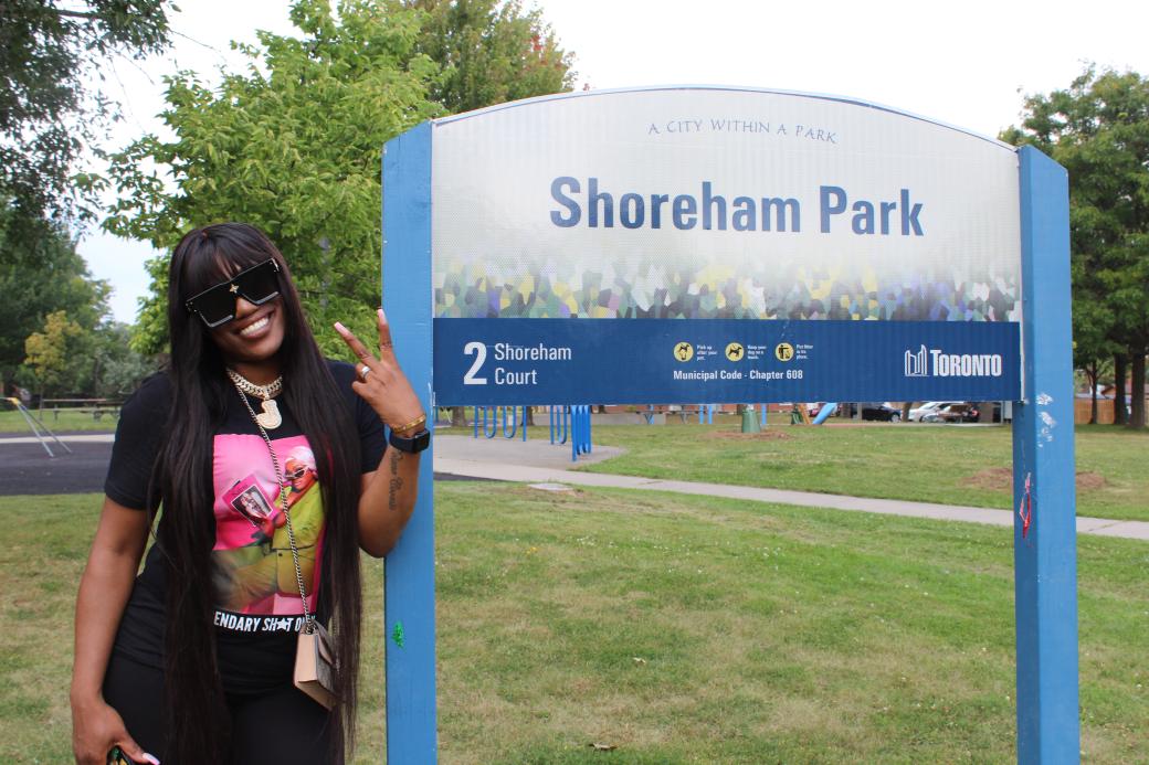 Woman posing in a park next to a sign that reads "Shoreham Park"