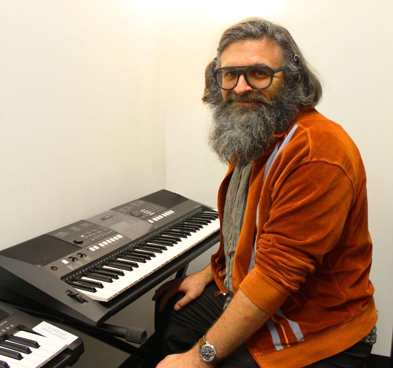 A man sitting in front of two keyboards in a plain beige room.