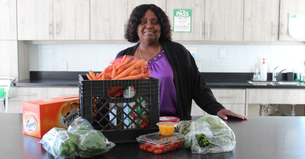 Lorraine Anderson standing behind a kitchen counter with various packaged food, vegetables and groceries laid out in front of her.