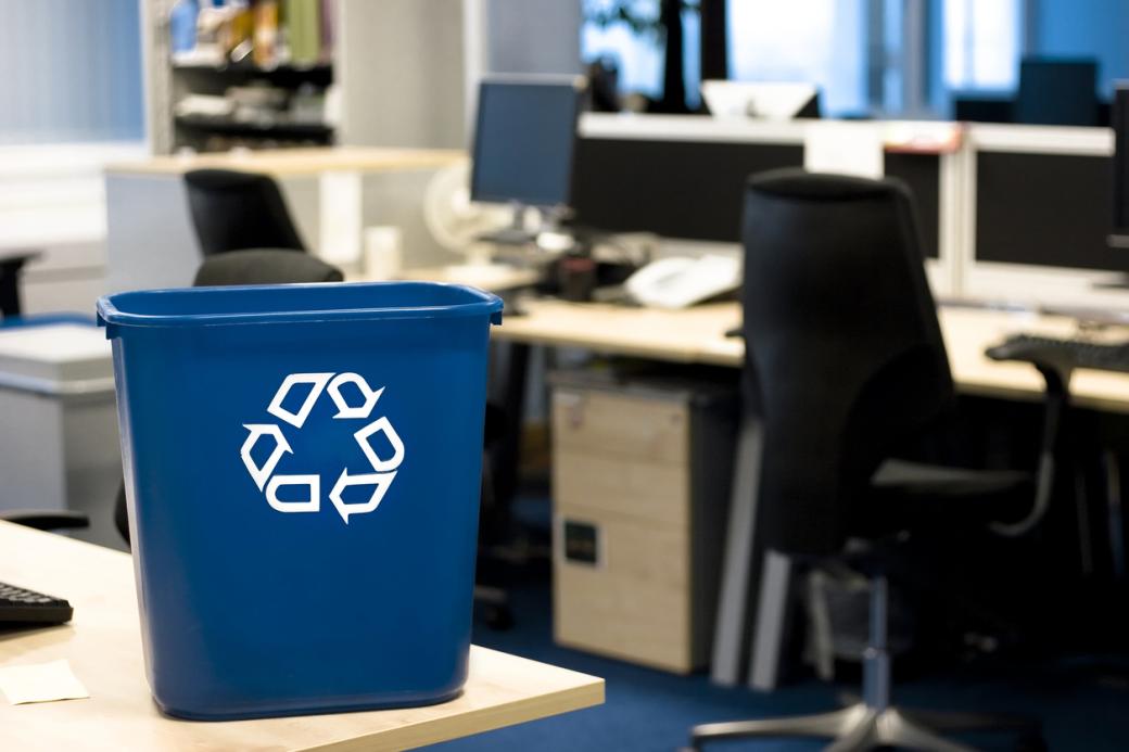 A blue recycling bin on top of a office desk. 