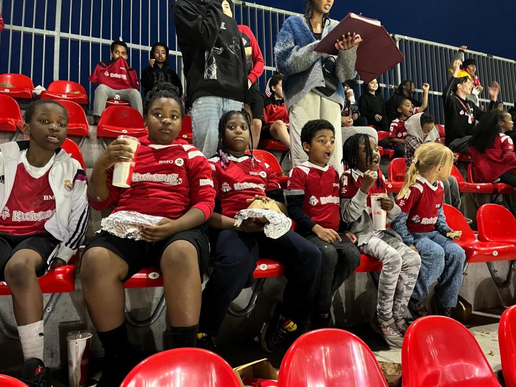 A group of kids wearing red KickStart shirts are watching the soccer match at BMO field. 