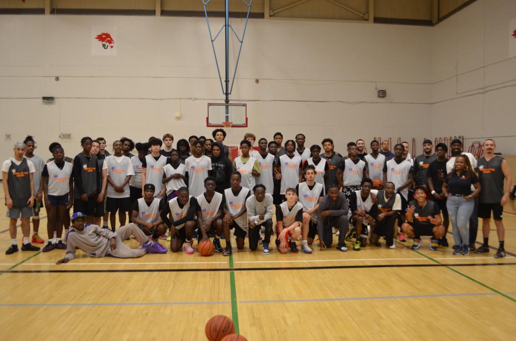 A group of people wearing basketball jerseys smile for a group photo on the basketball court. 