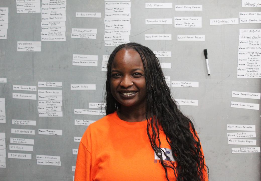 A person in an orange shirt standing against a grey wall