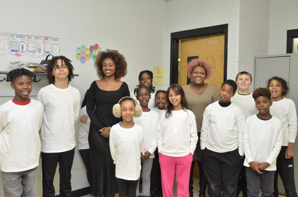 Two women and a group of children in white shirts smiling for the camera.