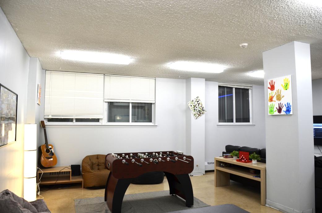 A room with paintings on the wall, a foosball table and a guitar in the corner.