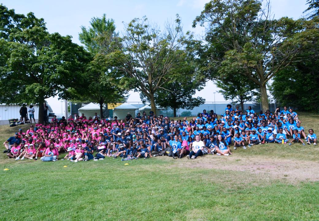 A group of children and adults sitting on a field smiling for the camera.