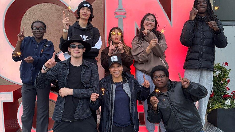 A group of people holding sparklers in front of a CN Tower sign
