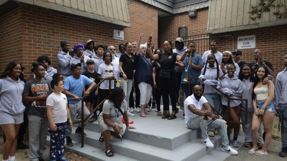 A group of people posing in front of a building while cutting a ribbon. 