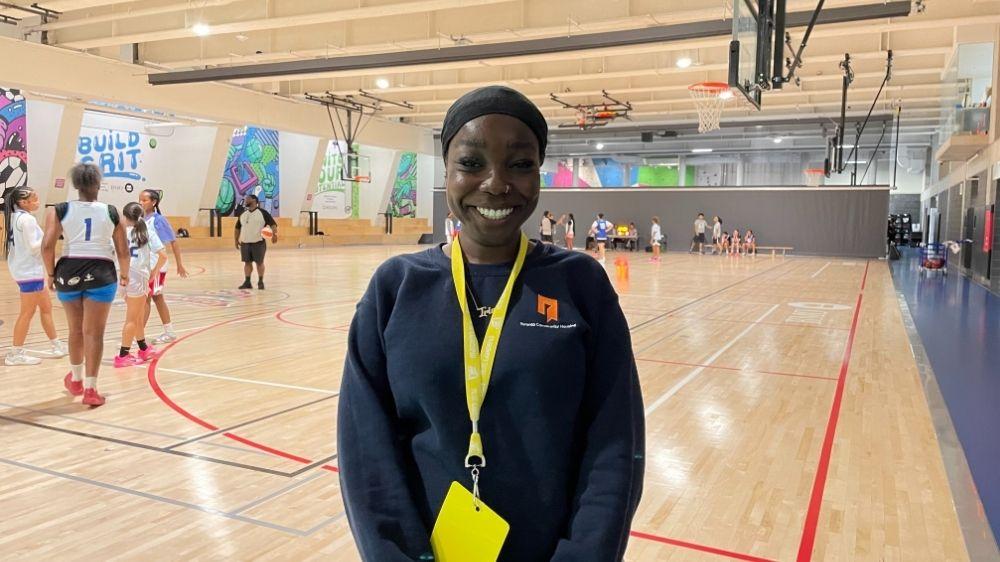 A girl wearing a blue TCHC sweatshirt standing in front of a basketball court.