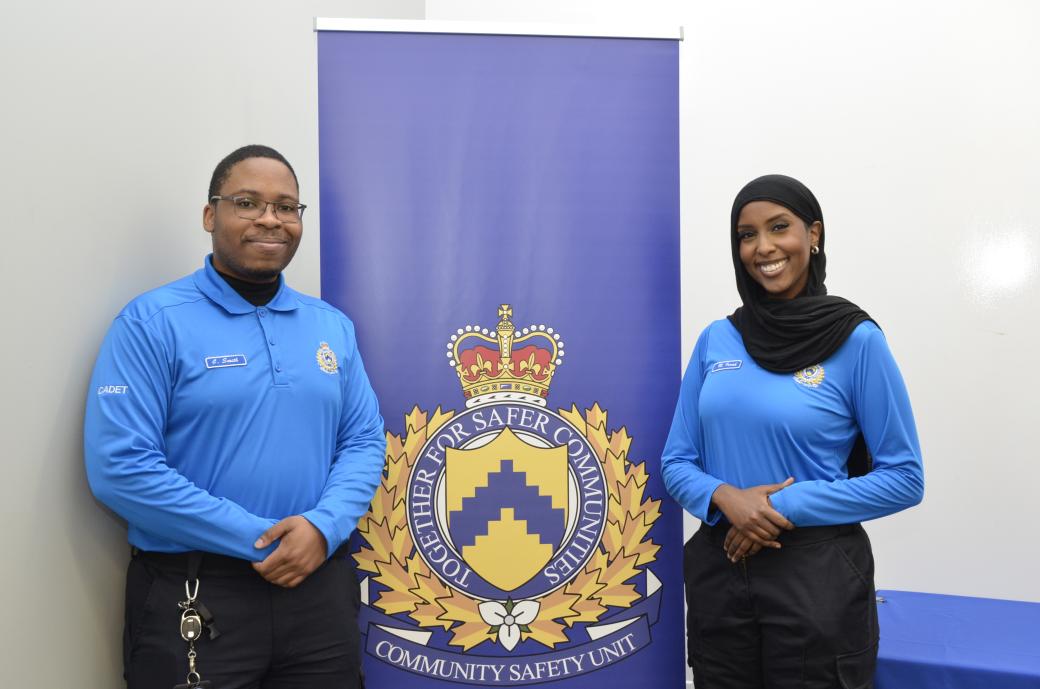 A photo of a young man and woman standing in front of the Community Safety Unit blue pop up banner. 